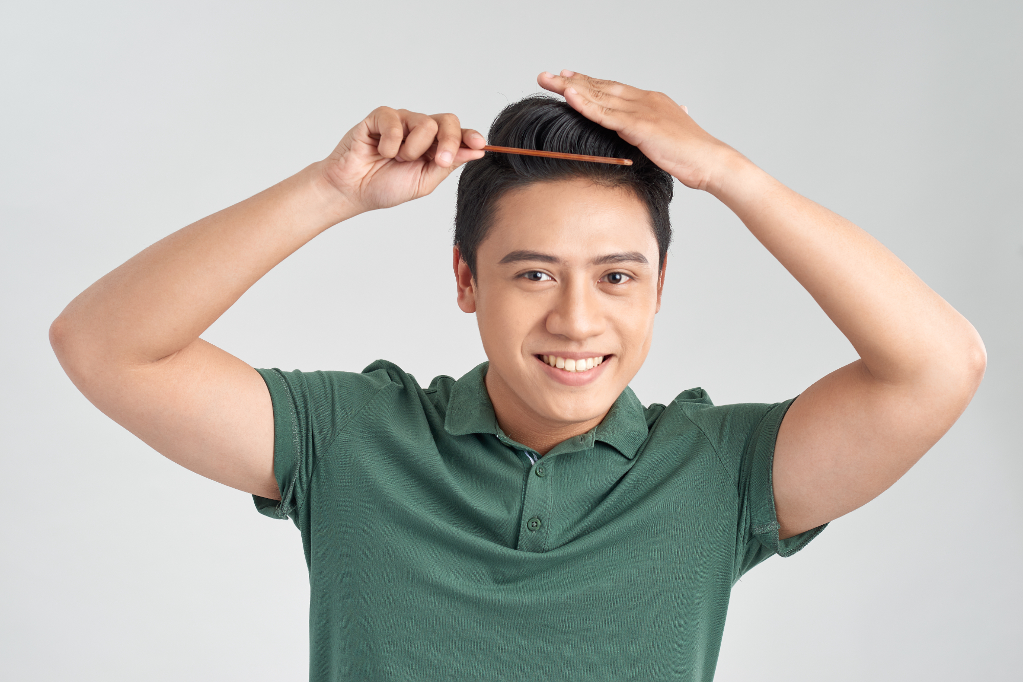 Smiling young man in a green polo shirt combing his dark hair.